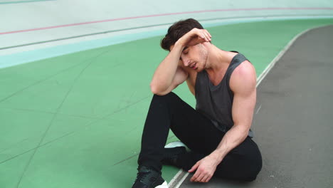 Closeup-man-resting-on-track.-Male-sitting-after-workout-on-athletics-track
