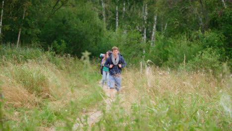 Group-of-tourists-with-backpacks-and-map-walk-along-path-among-dense-thickets