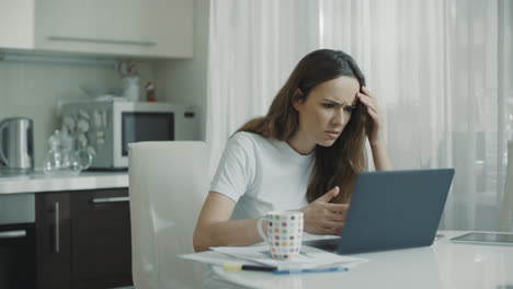 Angry-woman-typing-on-laptop-computer-at-kitchen.-Worried-woman-working-online