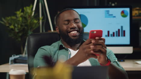 Closeup-joyful-afro-business-man-typing-message-on-smartphone-in-hipster-office