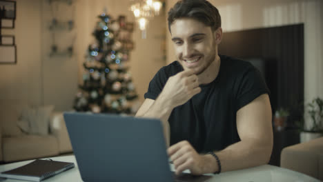 Hombre-Feliz-Trabajando-En-Una-Computadora-Portátil-En-Navidad.-Chico-Sonriente-Mirando-Computadora