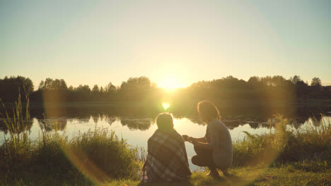Young-people-enjoy-rest-by-river-during-sunset.-Girls-with-guy-meet-dawn