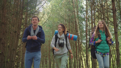 Jóvenes-Turistas-Con-Mochilas-Caminando-Por-El-Bosque-Riéndose-Unos-De-Otros