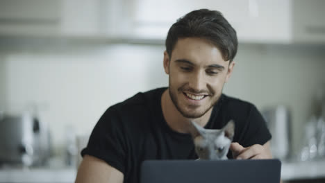 Hipster-man-touching-cat-at-home-workplace.-Happy-man-working-on-laptop
