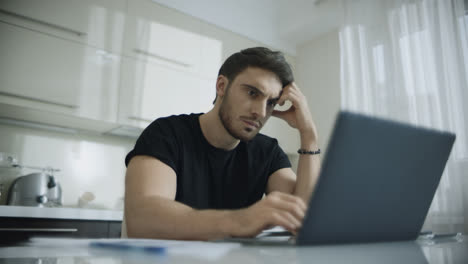 Young-man-typing-laptop-computer-at-home.-Pensive-businessman-using-computer