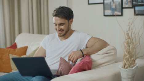 Smiling-man-looking-at-laptop-computer-at-home-sofa.-Pensive-guy-working-online