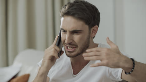 Unhappy-man-talking-mobile-phone-at-home.-Angry-person-scream-at-phone