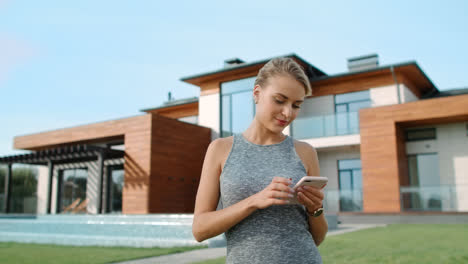 Relaxed-woman-texting-mobile-near-luxury-house.-Pretty-woman-standing-near-villa