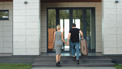 Traveler-couple-entering-hotel-back-view.-Modern-couple-coming-home-with-bag