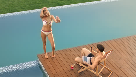Blonde-woman-taking-mobile-selfie-near-poolside.-Couple-relaxing-near-pool