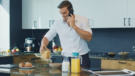Happy-man-preparing-breakfast-in-kitchen.-Relaxed-person-speaking-on-phone.