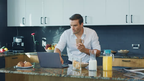 Smiling-man-watching-video-standing-in-kitchen.-Happy-person-scrolling-computer.
