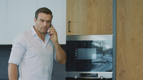 Business-man-talking-cell-phone-on-kitchen.-Man-having-telephone-call-in-house.