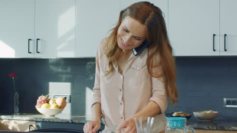 Happy-woman-preparing-breakfast-in-kitchen.-Joyful-person-speaking-on-mobile