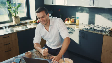 Business-man-talking-at-computer-in-kitchen.-Smiling-person-having-online-chat