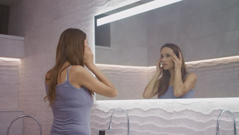Pretty-woman-massaging-face-in-bathroom.-Beautiful-woman-making-facial-yoga.