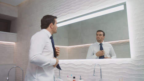 Business-man-setting-tie-in-luxury-bathroom.-Happy-man-wearing-necktie-in-house.