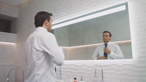 Business-man-wearing-tie-in-luxury-bathroom.-Happy-man-dressing-himself-in-house