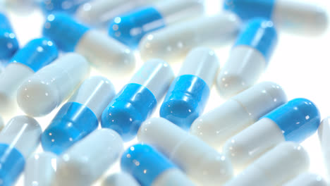 Medicine-pills.-Close-up-of-white-and-blue-capsules-rotating-on-white-table