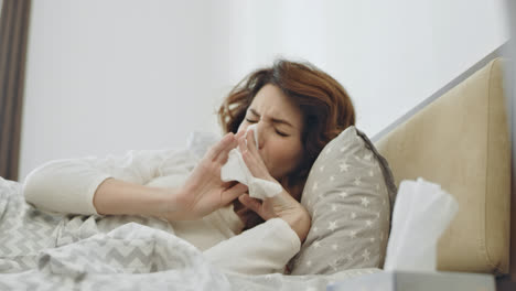 Ill-woman-getting-throat-virus-lying-in-bed.-Closeup-female-hands-taking-napkin