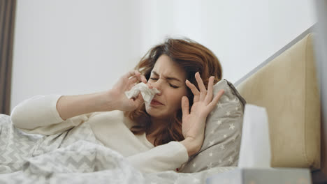 Sick-woman-feeling-bad-in-bedroom.-Ill-female-person-sneezing-in-bed.