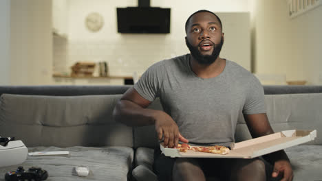 Hombre-Africano-Sentado-En-Un-Sofá-En-La-Cocina-Abierta.-Hombre-Negro-Comiendo-Pizza.