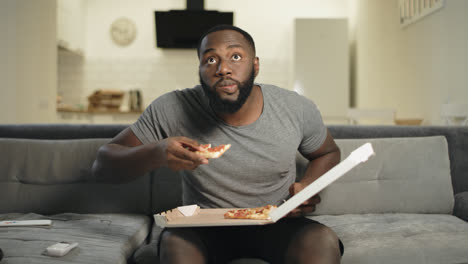 Concentrated-man-looking-at-tv-screen.-Happy-football-fan-biting-pizza.
