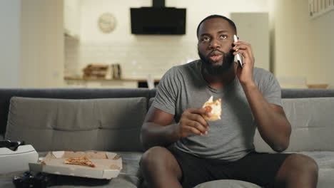Concentrated-man-talking-phone-with-pizza.-Black-man-watching-football-match.