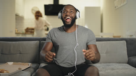 Hombre-Negro-Sorprendido-Escuchando-Música-En-La-Cocina-De-Casa-Con-Auriculares.