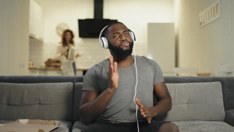 Black-man-dancing-at-home-with-rising-hands.-Funny-guy-sitting-in-headphones
