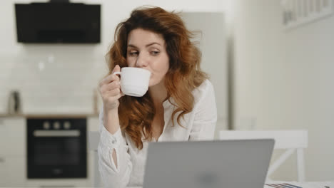 Happy-woman-working-laptop-at-remote-workplace.-Young-lady-drinking-tea-at-home.