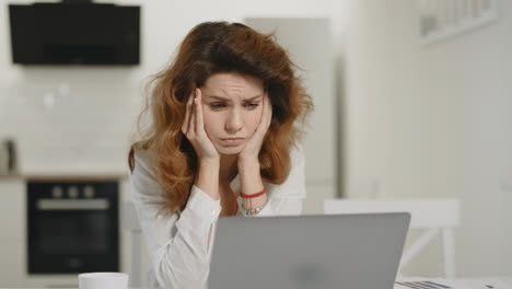 Frustrated-woman-working-computer-at-home.-Young-lady-staring-laptop-at-kitchen.