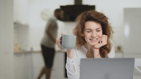 Smiling-woman-watching-funny-news-on-computer-at-open-kitchen.
