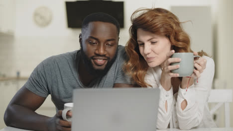 Happy-couple-talking-at-open-kitchen.-Smiling-man-and-woman-looking-at-laptop.