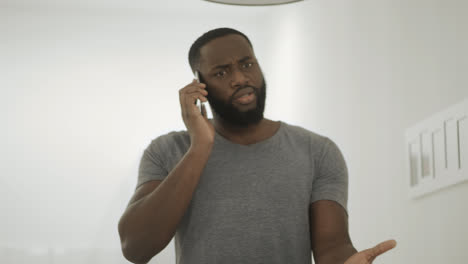 Serious-black-man-talking-phone-at-home-kitchen.-Young-guy-talking-smartphone