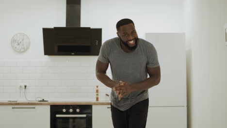 Joyful-black-man-clapping-hands-at-open-kitchen.-Happy-young-guy-dancing-at-home