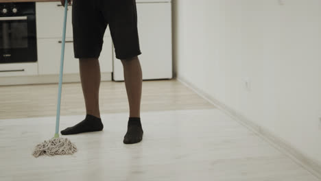 Black-man-cleaning-floor-at-kitchen-with-mop.-Serious-guy-washing-floor-in-socks