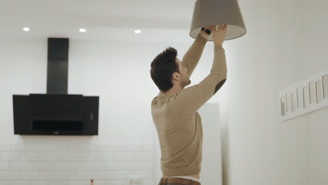 White-man-unscrewing-light-bulb-at-open-kitchen.-Guy-standing-under-chandelier