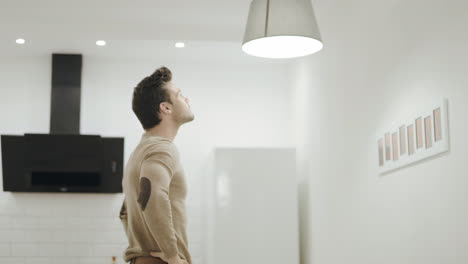 White-man-switching-off-chandelier-at-kitchen.-Young-guy-twisting-up-light-bulb