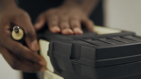Close-up-black-man-hands-unlocking-toolbox.-Man-worker-hands-taking-screw