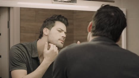 Handsome-man-looking-face-in-front-of-mirror.-Closeup-guy-adjusting-t-shirt