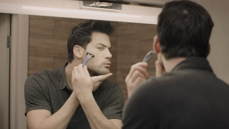 Young-man-shaving-face-in-front-of-mirror-at-bathroom.-Portrait-of-handsome-guy