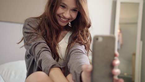 Young-woman-taking-selfie-photo-on-mobile-phone-at-bedroom