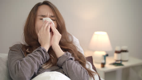 Sick-woman-sneezing-in-tissue-in-bed-at-evening.-Sick-girl-blowing-nose