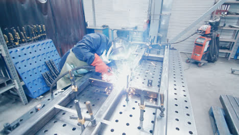 Worker-in-protective-suit-and-mask-conducting-metal-welding.-Factory-welder