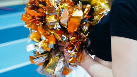 Girl-cheerleader-holding-pompoms-during-athletics-championship.-Motley-pompoms-in-hands