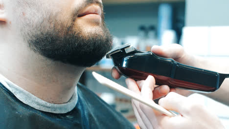 Hairdresser-cutting-beard-to-client-with-clipper.-Close-up-of-young-bearded-man