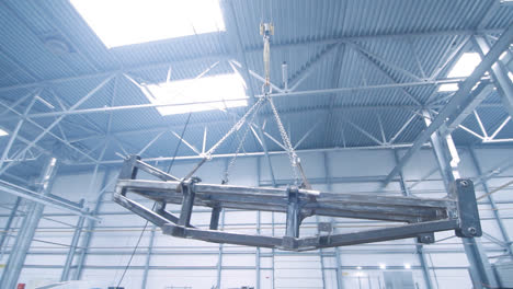 Hook-of-crane-with-chains-moving-big-metal-carcass-in-workshop