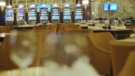 Empty-tables-with-wine-glasses-in-restaurant-near-slot-machines-in-casino