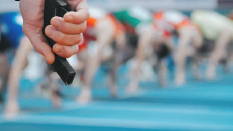 Referee's-hand-with-starting-pistol-on-blurred-background-of-athletes